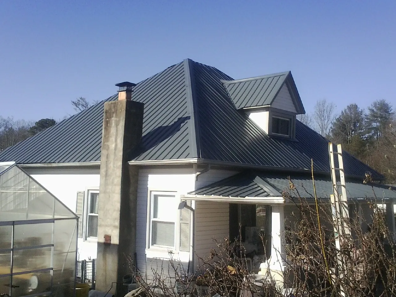 Dark blue standing seam metal roof on a white farmhouse with dormer — Slate & Tile Roof Repair by Roofing Brothers in Redlands