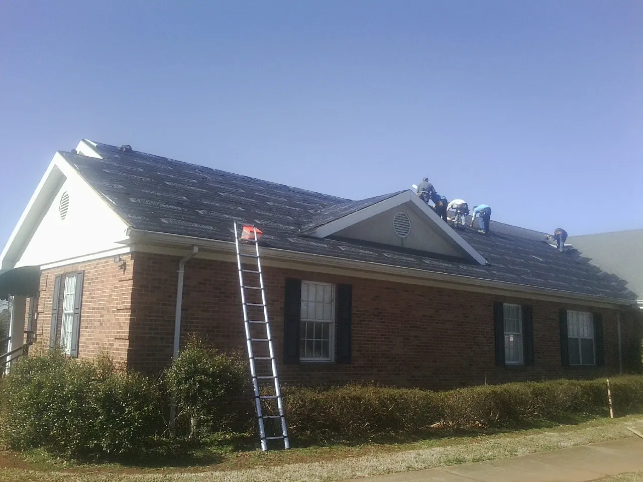 Crew tearing shingles off a brick ranch roof with a ladder set — Emergency Roof Repair work by our crew in Redlands