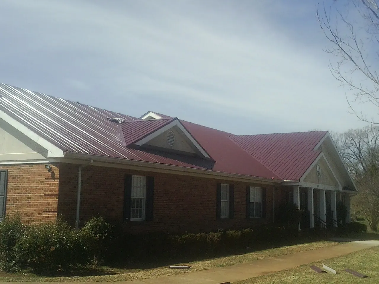 Red metal roof with gabled entries on a long brick building, from a Hail Damage Roof Repair job in Redlands