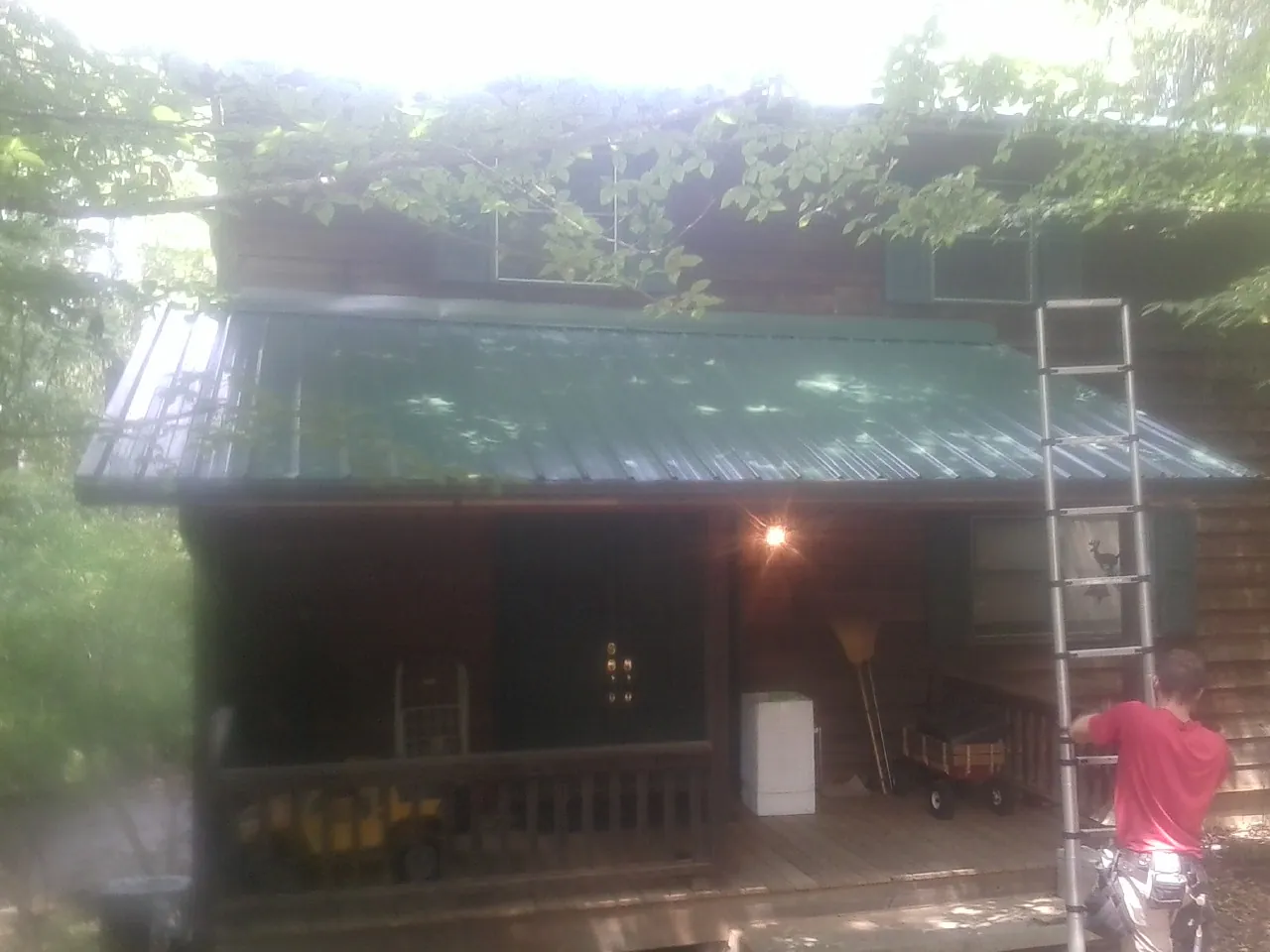 Worker on a ladder at the green porch roof of a wooded cabin in Redlands