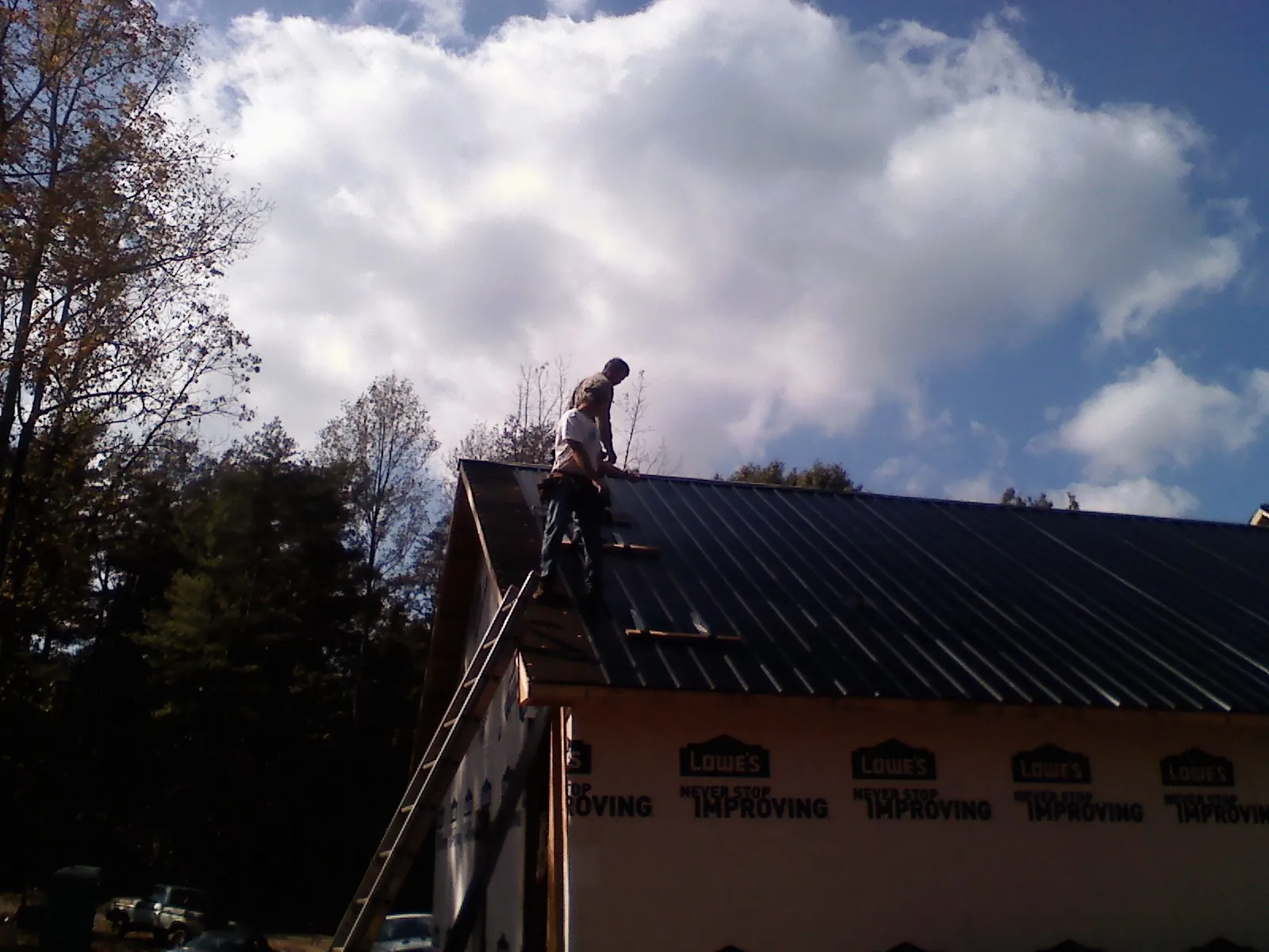 Roofer fastening dark metal panels high against a cloudy sky, from a Roof Inspection job in Redlands
